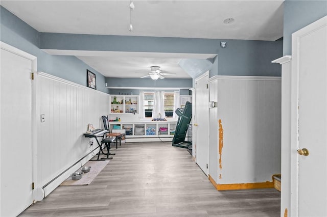 workout room featuring ceiling fan, wood finished floors, and a wainscoted wall