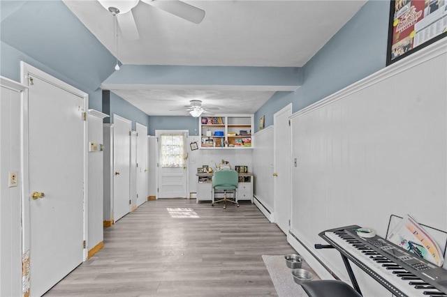 interior space with built in study area, light wood-style flooring, ceiling fan, and baseboard heating