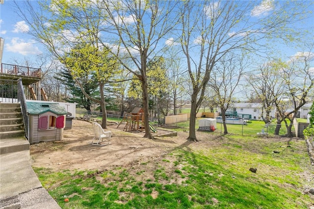 view of yard with a playground, fence, stairway, and a deck