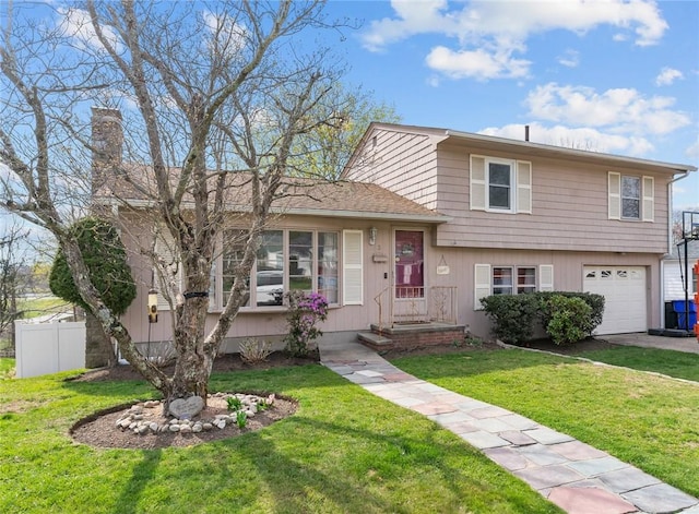 split level home with driveway, a chimney, a front yard, a garage, and fence