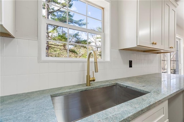 kitchen with a sink, decorative backsplash, light stone countertops, and white cabinets
