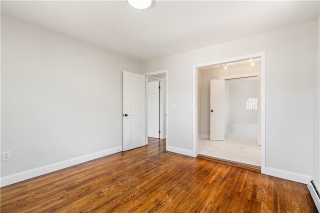 unfurnished bedroom featuring baseboards, a baseboard heating unit, and wood finished floors