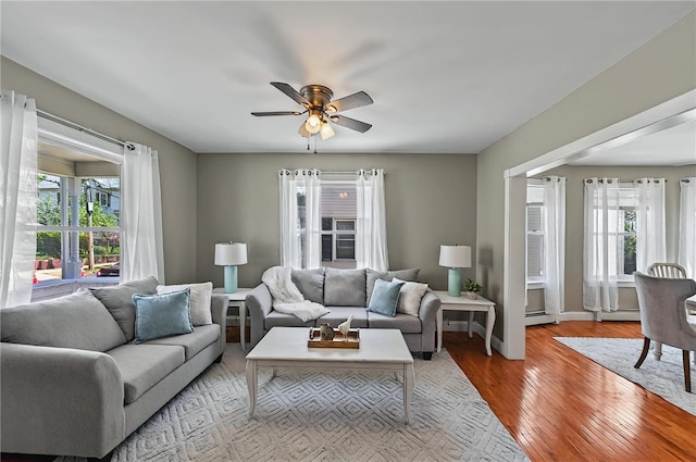 living room featuring a baseboard heating unit, ceiling fan, wood finished floors, and a healthy amount of sunlight