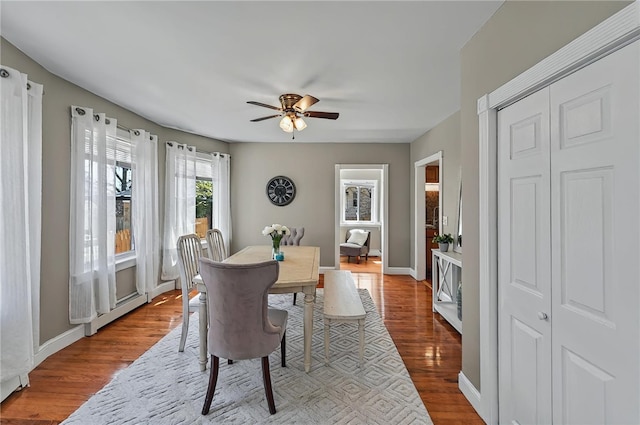 dining space featuring baseboards, a ceiling fan, a baseboard heating unit, and wood finished floors