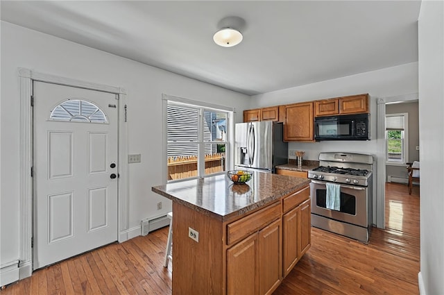 kitchen with brown cabinetry, wood finished floors, a kitchen island, a baseboard radiator, and appliances with stainless steel finishes