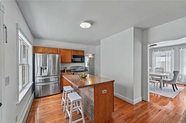kitchen with black microwave, stainless steel fridge with ice dispenser, brown cabinetry, gas range, and a baseboard heating unit