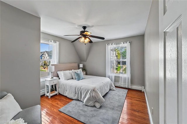 bedroom with multiple windows, wood finished floors, and a baseboard radiator