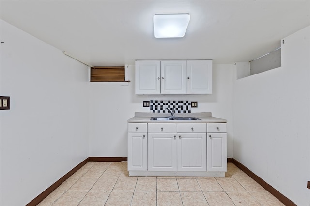 kitchen featuring light tile patterned flooring, baseboards, light countertops, white cabinets, and a sink