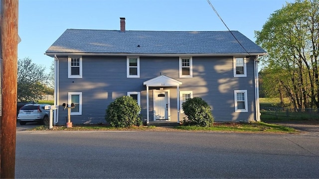 colonial inspired home featuring fence, a chimney, and roof with shingles