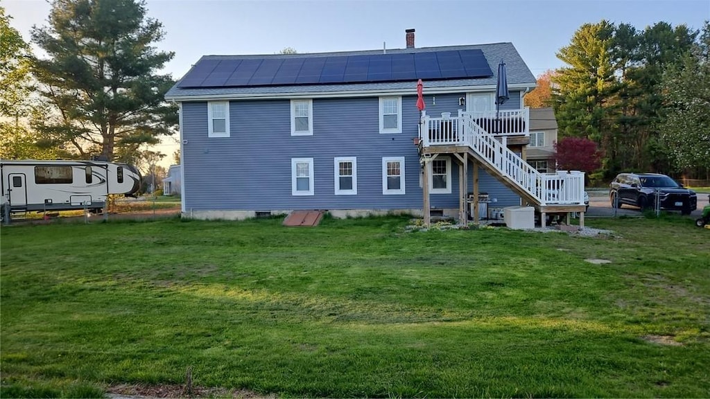 rear view of property featuring roof mounted solar panels, a wooden deck, a yard, and stairway