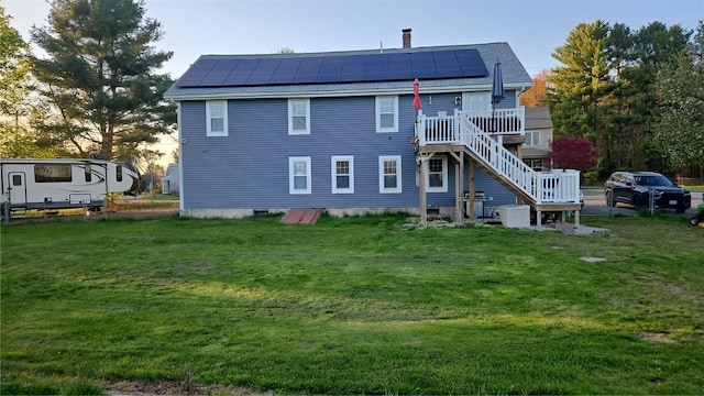rear view of property featuring roof mounted solar panels, a wooden deck, a yard, and stairway