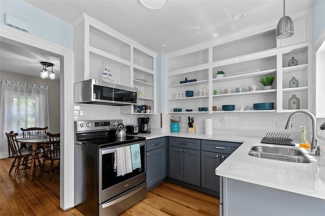 kitchen with appliances with stainless steel finishes, open shelves, a sink, light stone counters, and light wood-style flooring