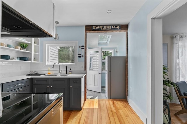 kitchen with exhaust hood, a sink, gray cabinetry, freestanding refrigerator, and a wealth of natural light