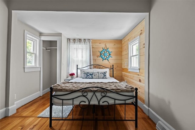 bedroom featuring baseboards, wood finished floors, wooden walls, and a closet