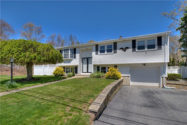 bi-level home featuring fence, driveway, a front lawn, and a garage