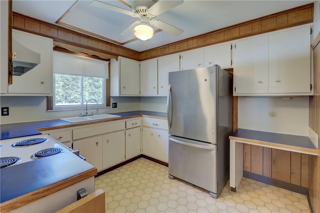 kitchen with freestanding refrigerator, ceiling fan, wall chimney range hood, white cabinets, and a sink