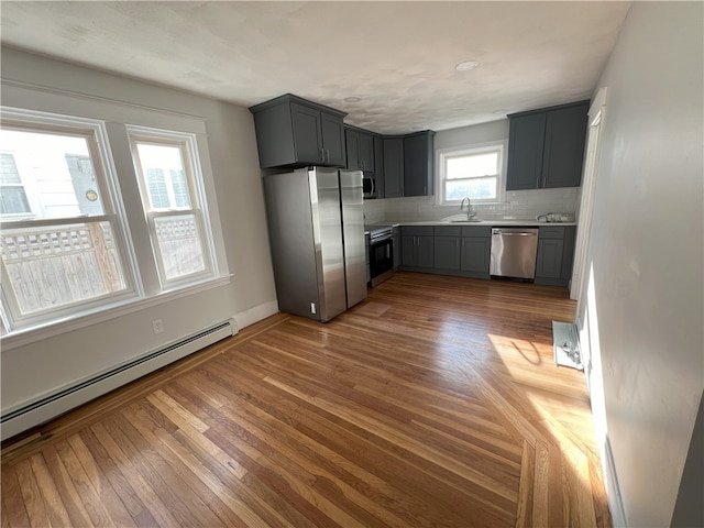 kitchen featuring a sink, light countertops, a baseboard radiator, appliances with stainless steel finishes, and backsplash