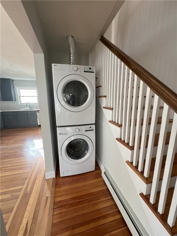 laundry room featuring laundry area, baseboard heating, a sink, light wood-style floors, and stacked washer and clothes dryer