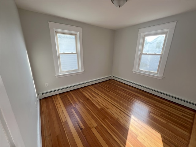 empty room featuring a baseboard heating unit, a wealth of natural light, and hardwood / wood-style floors
