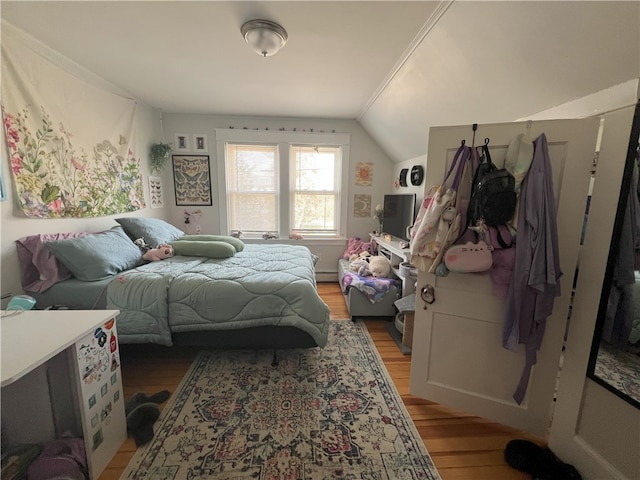 bedroom with a baseboard heating unit, light wood-style flooring, and lofted ceiling