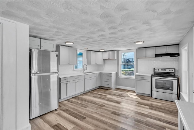 32 Summer St, Woonsocket, RI 02895 - kitchen with light countertops, under cabinet range hood, light wood finished floors, appliances with stainless steel finishes, and gray cabinetry