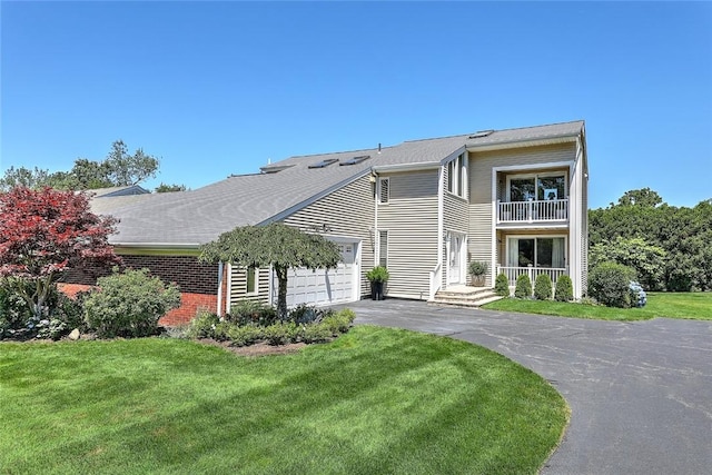 view of front of house with driveway, a garage, brick siding, a balcony, and a front lawn