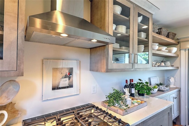 kitchen featuring light countertops, glass insert cabinets, and wall chimney exhaust hood