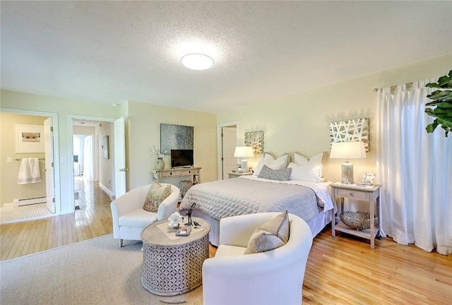 bedroom featuring a textured ceiling, light wood finished floors, and a baseboard heating unit