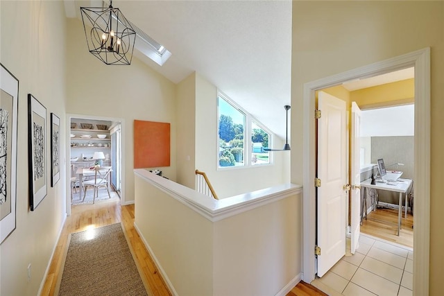 corridor with an inviting chandelier, baseboards, high vaulted ceiling, light wood-type flooring, and a skylight