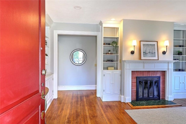 living area with baseboards, built in shelves, wood finished floors, and a fireplace