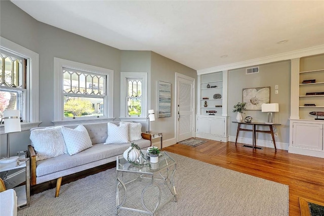 living area featuring baseboards, visible vents, built in shelves, and wood finished floors