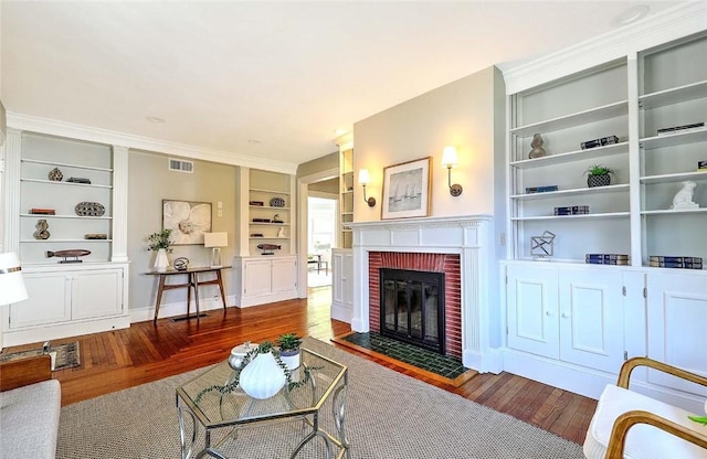 living area featuring visible vents, ornamental molding, built in features, a brick fireplace, and hardwood / wood-style floors