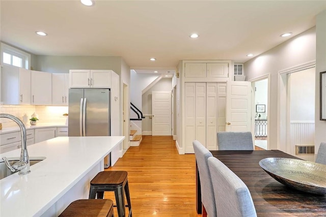 kitchen with freestanding refrigerator, recessed lighting, white cabinetry, light wood-type flooring, and a kitchen bar
