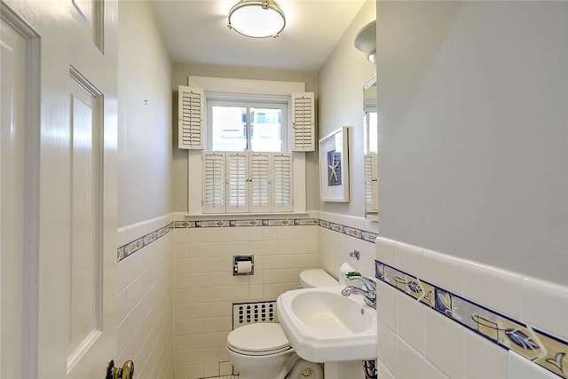 bathroom with a sink, wainscoting, toilet, and tile walls