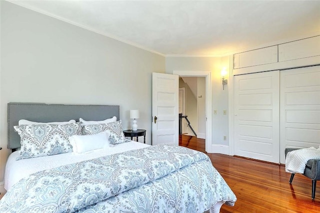 bedroom with crown molding, baseboards, a closet, and wood finished floors