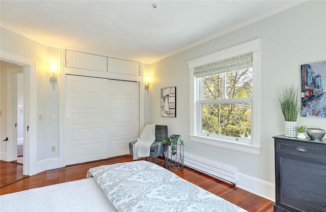 bedroom with a baseboard heating unit, ornamental molding, wood finished floors, and a closet