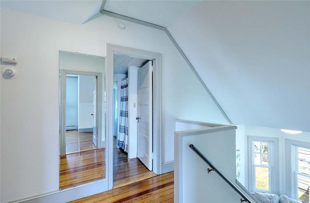 hallway featuring lofted ceiling, a baseboard heating unit, wood finished floors, and an upstairs landing
