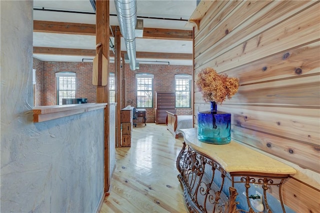 hallway featuring brick wall, plenty of natural light, wood finished floors, and beam ceiling