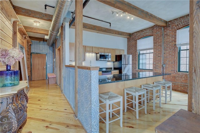 kitchen featuring brick wall, beamed ceiling, a kitchen breakfast bar, light wood-type flooring, and appliances with stainless steel finishes