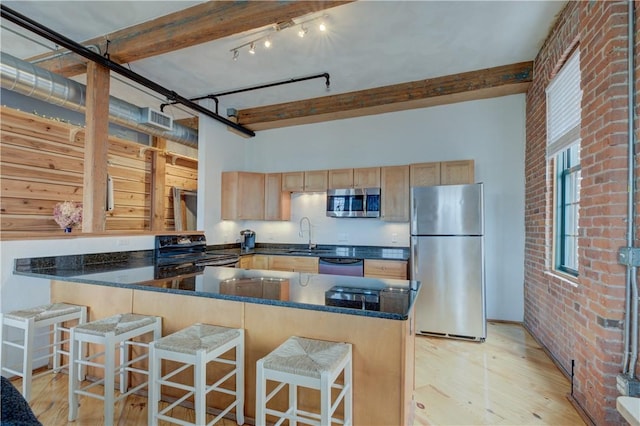 kitchen with light wood-style floors, light brown cabinetry, stainless steel appliances, and dark stone countertops