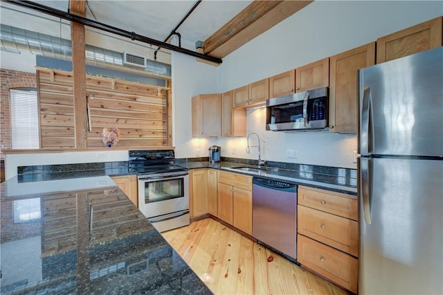 kitchen with visible vents, a sink, light wood finished floors, dark stone counters, and stainless steel appliances