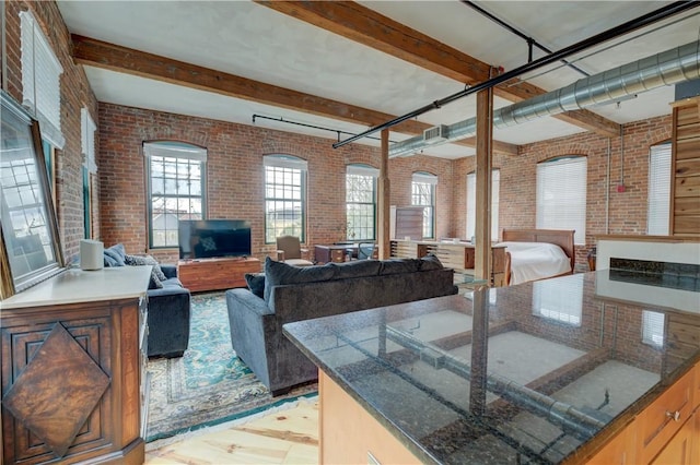 kitchen featuring beamed ceiling, brick wall, open floor plan, and dark stone countertops