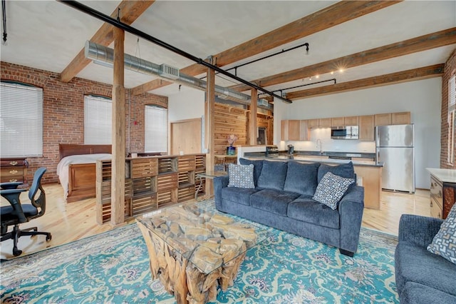 living area with brick wall, visible vents, beam ceiling, and light wood finished floors