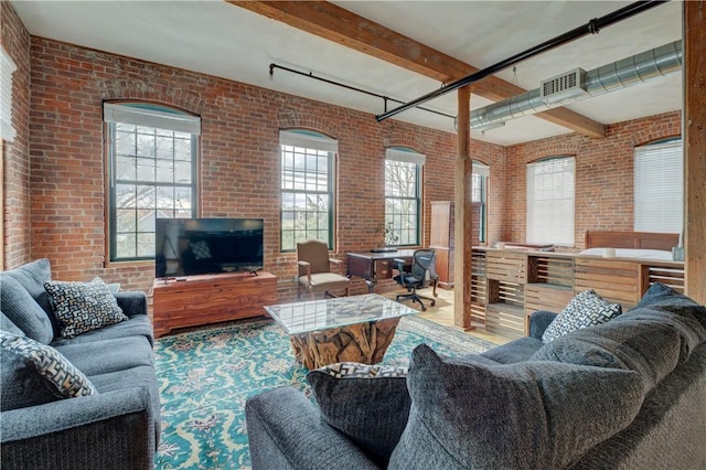 living area featuring a healthy amount of sunlight, beamed ceiling, brick wall, and visible vents