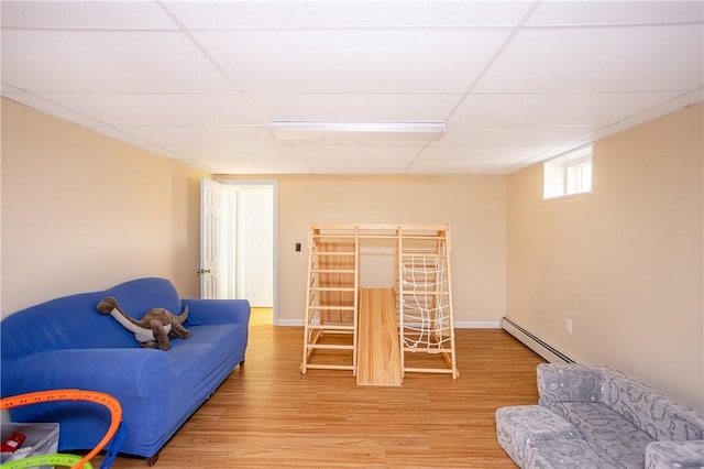 living area with light wood-style flooring, a paneled ceiling, and a baseboard heating unit