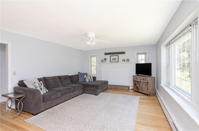 living area with light wood-style floors, a baseboard radiator, and ceiling fan