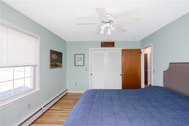 bedroom featuring a closet, baseboards, ceiling fan, a baseboard heating unit, and light wood-style flooring