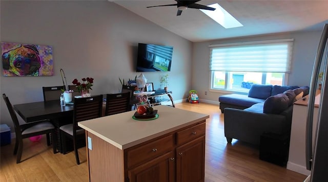 living room featuring baseboards, a ceiling fan, light wood-style flooring, and vaulted ceiling with skylight