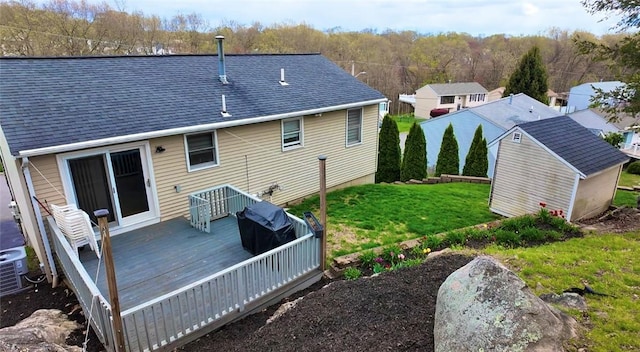 rear view of property featuring a shingled roof, a wooden deck, a shed, an outbuilding, and a lawn