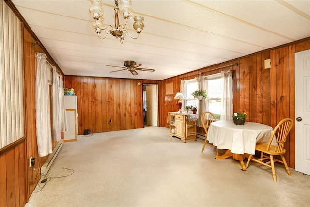dining room featuring wooden walls, light colored carpet, baseboard heating, ceiling fan with notable chandelier, and a baseboard heating unit